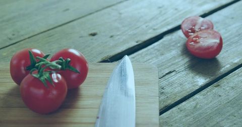 Showing vine tomatoes on cutting board with chef knife and halved tomato closeup