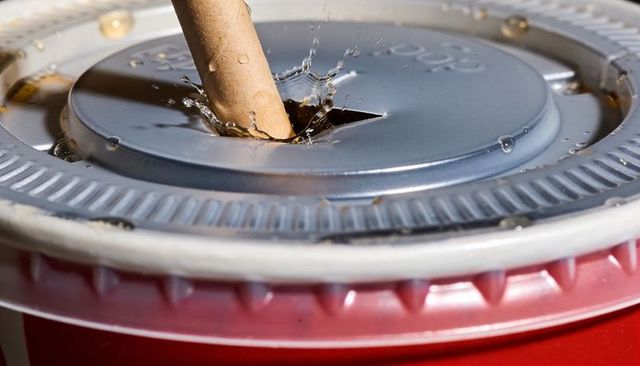 Macro splashing cola in red disposable cup with paper straw and gray sip lid