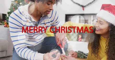 Couple wrapping christmas gifts at home, woman in santa hat helping with ribbon and scissors