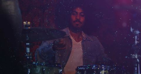 Indian drummer performing on stage in denim jacket white tee neon purple lighting