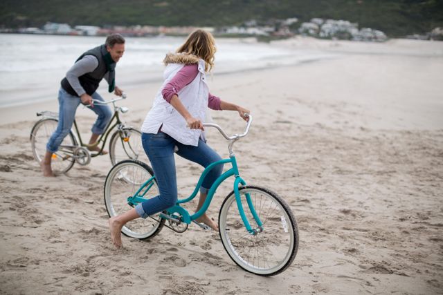 Mature couple enjoying a fun and active day riding bicycles on a sandy beach. Ideal for promoting outdoor activities, healthy lifestyles, vacation destinations, and family bonding experiences.