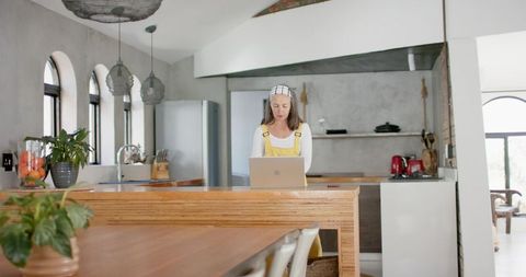 Mature woman working on laptop at wooden kitchen island in modern rustic home office