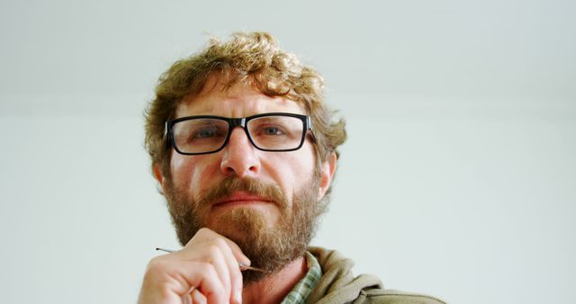 A middle-aged Caucasian man with a beard and glasses appears contemplative, with copy space. His thoughtful expression and casual attire suggest a moment of reflection or decision-making.