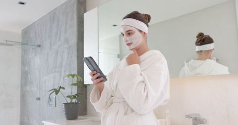 Woman in Bathroom Wearing Face Mask Using Smartphone
