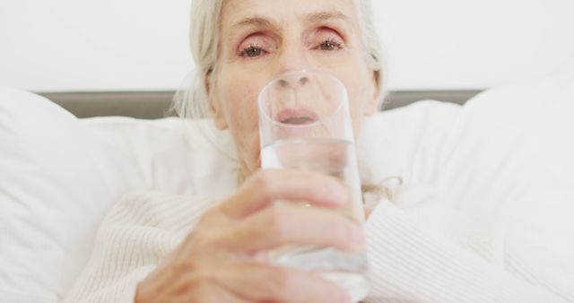 Image of caucasian senior woman drinking water in bed. retirement, well being and senior lifestyle concept.