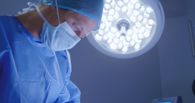 A surgeon is performing a procedure in an operating room. He is dressed in blue scrubs and a mask, demonstrating concentration in a sterile environment. Useful for illustrating surgical procedures, hospital scenes, medical blogs, and healthcare services.