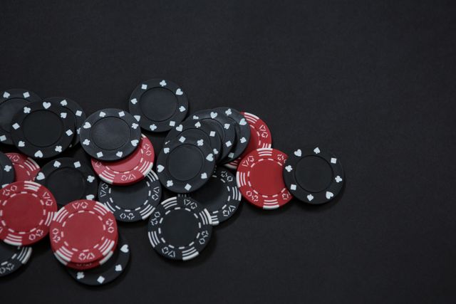 High angle view of red and black casino chips scattered on a black table. Ideal for use in articles or advertisements related to gambling, poker games, casino nights, or betting strategies. Perfect for illustrating gaming concepts or casino-themed events.