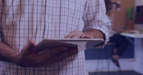 Man tapping tablet at coworking counter wearing white blue-grid button-up shirt for office