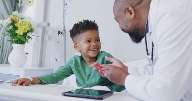 Pediatric doctor interacting with a young boy in hospital room, both smiling and sharing a happy moment. Could be used in healthcare websites, pediatric care promotions, or educational materials about child health and doctor-patient relationships.