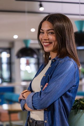 Young woman smiling with arms crossed in modern coworking space, casual denim style