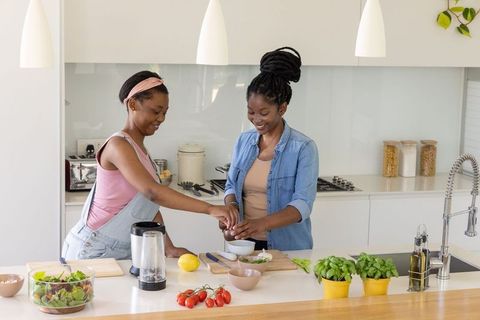 African woman and girl preparing healthy meal in bright modern kitchen, teamwork cooking