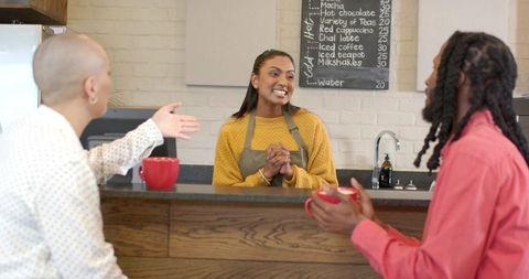 Smiling woman barista engaging with customers at cozy coffee counter with chalkboard menu