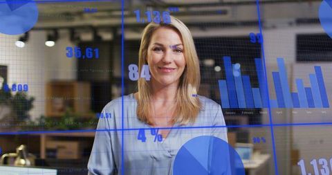 Confident mature blonde businesswoman presenting blue data charts on glass office dashboard