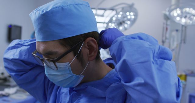 Asian male surgeon wearing face mask, putting surgical cap on in operating theatre - Download Free Stock Photos Pikwizard.com