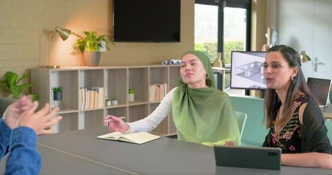 Diverse coworkers collaborating in modern office with indian woman in green hijab taking notes