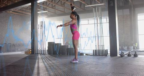Athletic woman pressing kettlebell overhead during strength training in warehouse gym