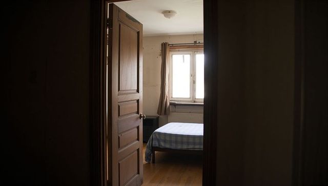 Opening paneled door revealing sunlit bedroom with checkered bedspread and hardwood floor