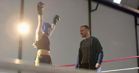 Female boxer celebrating victory with coach in boxing ring under dramatic gym lighting
