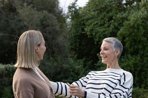 Senior woman and younger friend smiling and holding hands in peaceful garden