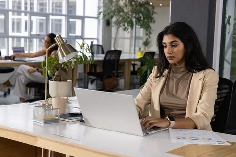 Indian professional woman working on laptop in modern open-plan office