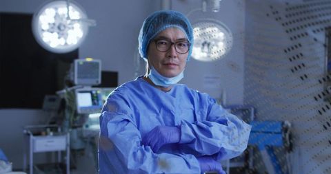 Standing surgeon crossing arms in operating room wearing blue surgical gown cap and gloves