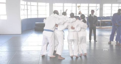 Martial arts team celebrating victory, lifting trophy together in bright dojo