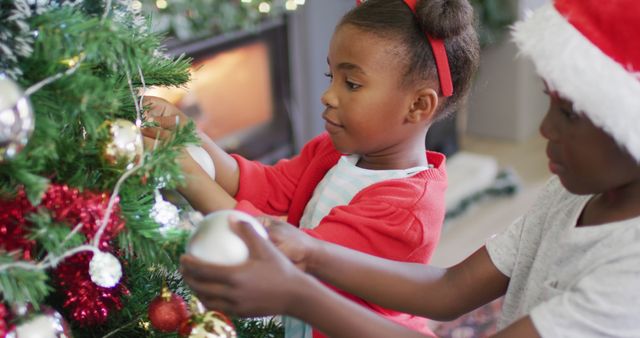 Two children are engaging in holiday decoration by adorning a Christmas tree with colorful ornaments. The scene exudes a festive and joyful atmosphere. This image is perfect for use in holiday-related content, family and seasonal campaigns, or promotions emphasizing Christmas traditions and family togetherness.