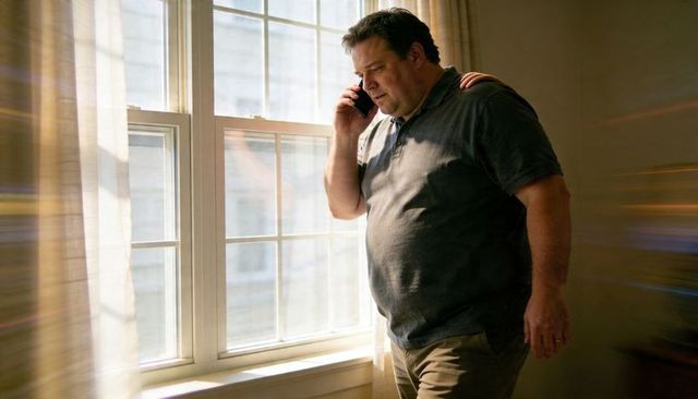 Contemplative man using smartphone by sunlit window with soft curtains and lensflare