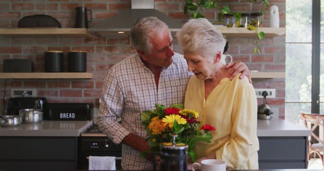 This captures a happy senior couple standing in their modern kitchen, with the man tenderly embracing the woman while she holds a vibrant bouquet of flowers. Ideal for personal care services, advertising retirement communities, romantic greeting cards, or lifestyle blogs focusing on senior living and love in later life.