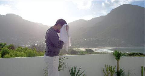 Man wiping face with towel on coastal terrace overlooking bay and mountains at sunrise