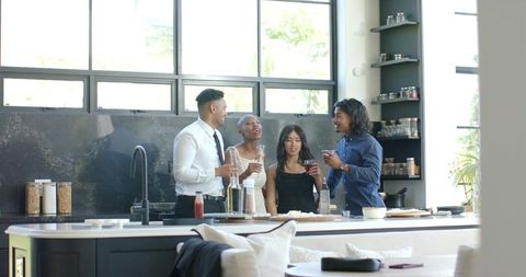 Multicultural friends gathering at modern kitchen island enjoying drinks and conversation