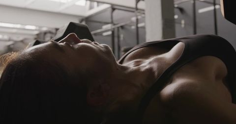 Strong female athlete bench pressing in gym environment