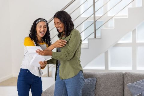 Diverse mother and daughter celebrating while opening good news mail in modern living room