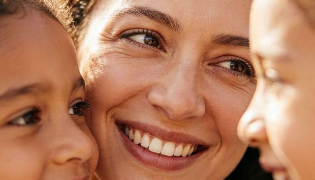 Smiling mother leaning between children during sunlit golden hour close-up