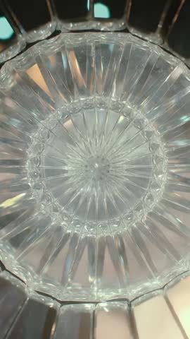 Vertical macro video of crystal tumbler rotating with teal and amber light creating starburst