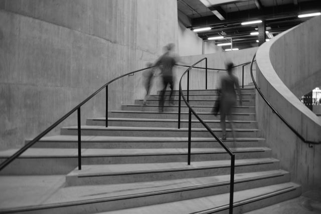 Modern architectural staircase with people climbing in motion blur, creating a dynamic feeling. Suitable for illustrating modern design, urban settings, or movement. Could be used in articles about architecture, urban environments, or human activity in public spaces.