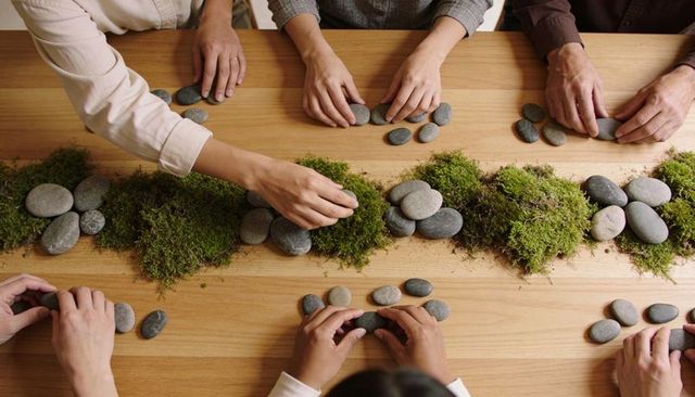 Hands arranging river stones and moss on wooden table for collaborative mindfulness workshop