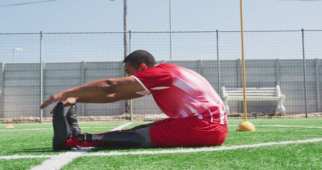 Disabled biracial male football player, stretching on outdoor pitch. Football, sports, fitness, disability and inclusivity.