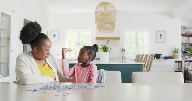 Happy african american granddaughter and grandmother doing jigsaw puzzle at home, copy space. Science, education, learning, family and domestic life.