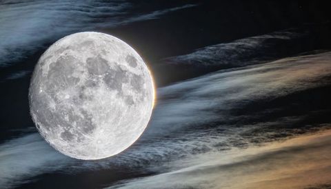 Full moon dominating night sky, casting halo through thin cirrus cloud bands, showing lunar craters