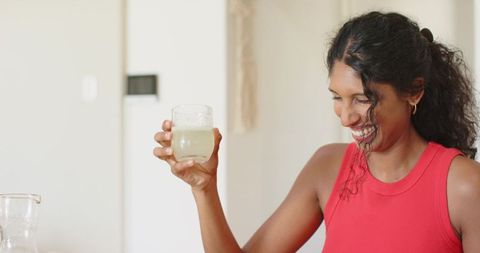 African american woman holding glass and smiling in bright kitchen lifestyle moment
