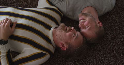 Happy caucasian gay couple lying together on carpet smiling