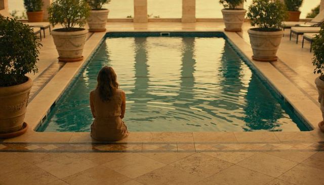 Woman sitting by ornamental pool dipping feet on mediterranean-style terrace with columns, planters