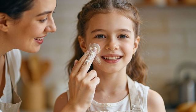 Mother dabbing flour on daughter's cheek while baking together in cozy home kitchen