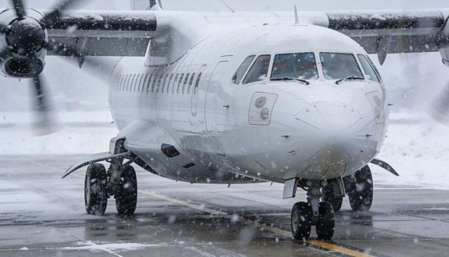 Turboprop airliner taxiing through heavy snow on airport tarmac with spinning propellers
