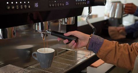 Diverse baristas pulling espresso shot with portafilter at cafe counter
