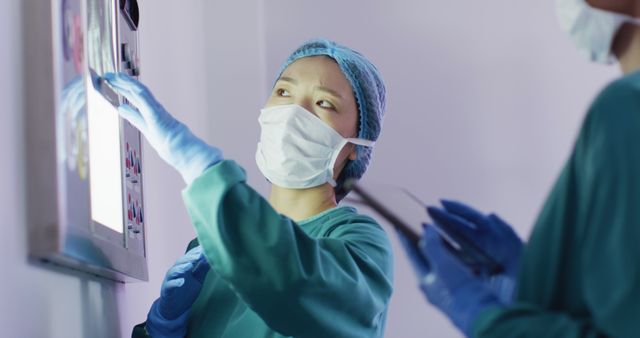 Image of asian female surgeon discussing x-ray with colleague in operating theatre. Hospital, medical and healthcare services.