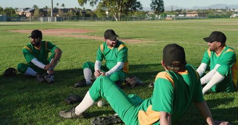 Green Uniform Baseball Team Sitting on Outfield Grass Chatting and Preparing for Game