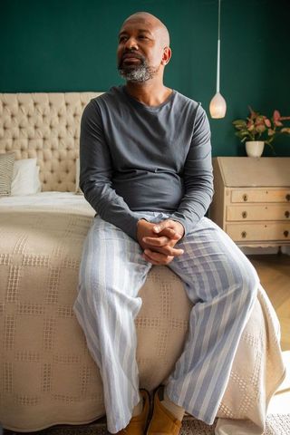 Mature african american man sitting on bed wearing striped pajama pants, quiet morning