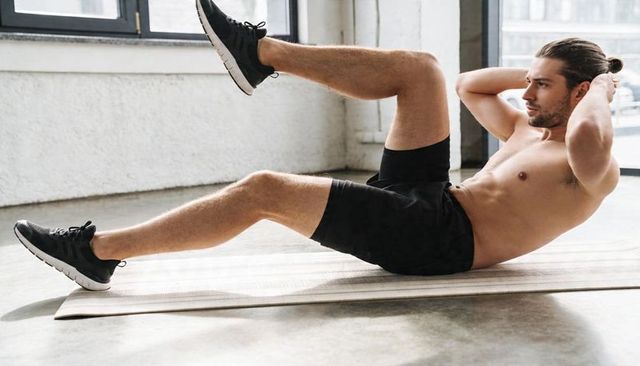 Shirtless athletic man performing bicycle crunches on exercise mat in urban loft studio